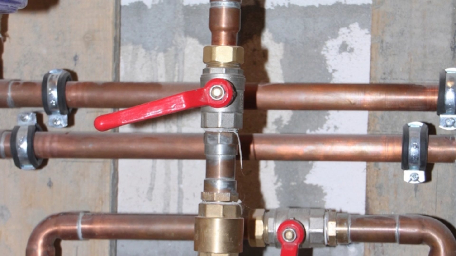 Copper water pipes with red-handled shut-off valves (illustrative stock photograph)